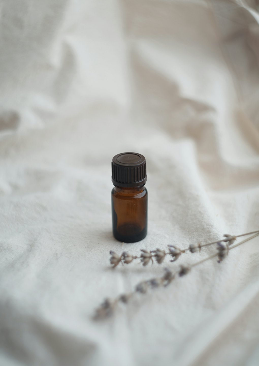 Bernsteinfarbene ätherische Ölflasche auf weißem Stoff mit Lavendel.